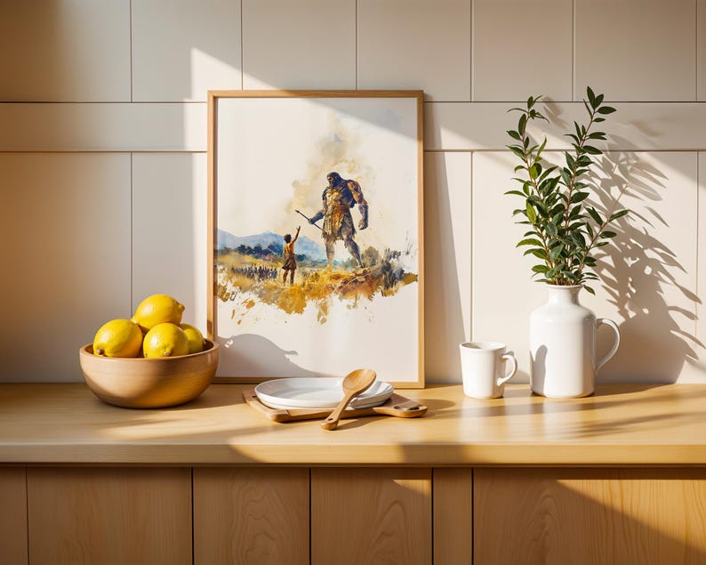 May include: A framed watercolor print depicting a small figure reaching toward a giant, displayed on a wooden counter next to a bowl of yellow lemons, a white plate with a wooden spoon, a white mug, and a white vase containing green leafy branches.