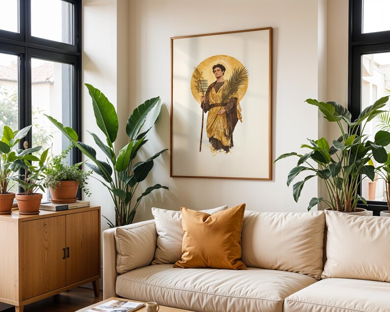 Op de afbeelding: Een ingelijste kunstdruk met een klassieke illustratie van een figuur in gouden gewaden die een palmtak en een staf vasthoudt, tegen een achtergrond van een cirkelvormige gouden halo, weergegeven in een kamer met een beige bank en groene planten.