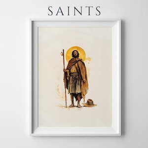 May include: A framed wall art print featuring the text SAINTS at the top. The illustration depicts a bearded figure in tan and brown robes holding a wooden staff, standing before a golden halo. A wide-brimmed hat rests on the ground nearby.