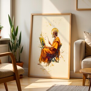 May include: A framed vertical wall art print featuring a watercolour-style illustration of a bearded figure in orange robes sitting on a chair, holding a paintbrush and a small framed portrait of a person with a halo against a cream background.