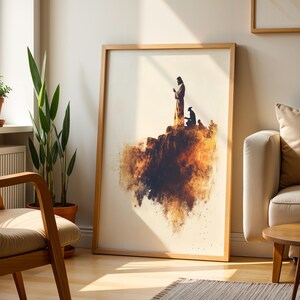 K&ouml;nnte beinhalten: Ein gerahmter Wandkunstdruck mit der Silhouette einer stehenden und einer knienden Figur auf einer felsigen Klippe, gestaltet in warmen orangefarbenen, braunen und schwarzen Aquarell-Spritzern auf cremefarbenem Hintergrund.
