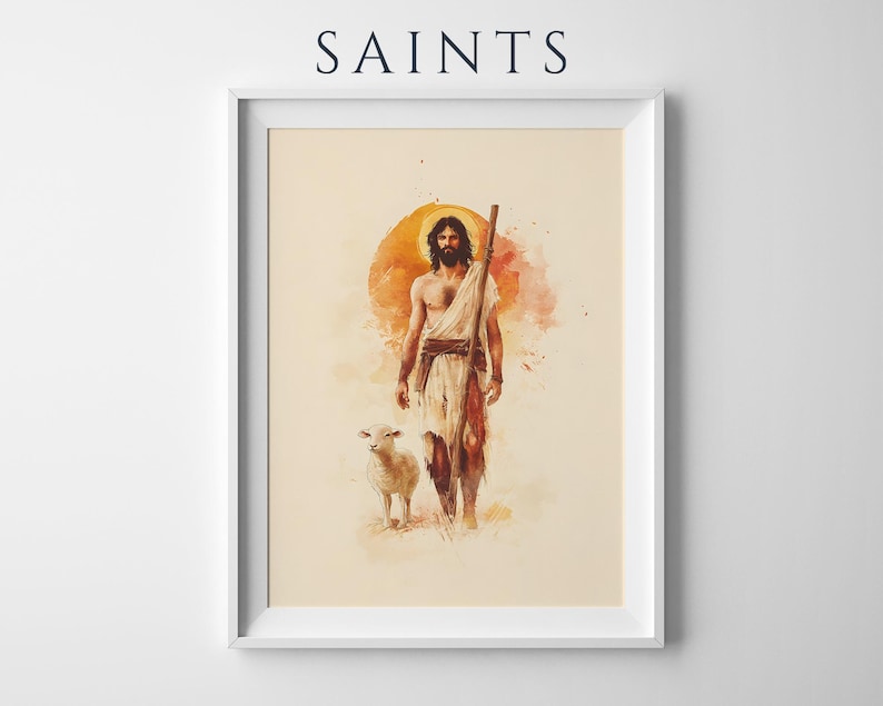 May include: A framed art print titled SAINTS featuring a watercolor illustration of a bearded figure in a white robe holding a wooden staff, accompanied by a small lamb. The background displays a warm orange circular sun motif on a cream field.