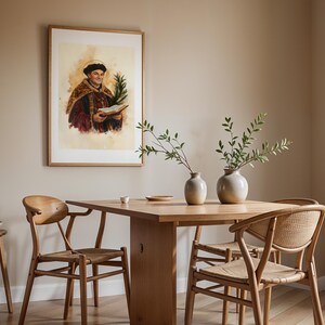 May include: A framed watercolor-style portrait of a figure in historical robes holding a book and a palm frond, displayed above a light wood dining table with two ceramic vases containing green branches and two wooden chairs with woven seats.