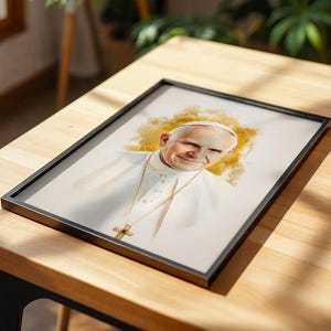 May include: A framed portrait print featuring a watercolour-style illustration of Pope John Paul II wearing a white cassock and a gold crucifix necklace, set against a soft, golden-yellow circular halo effect on a light, neutral background.