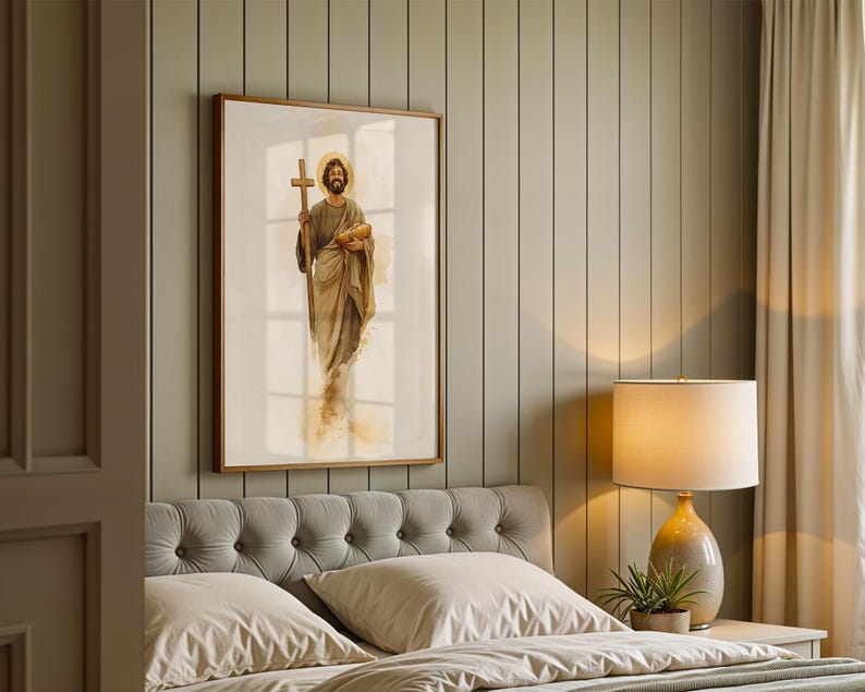 Op de afbeelding: Een ingelijste wandkunstprint met een aquarelillustratie van een bebaarde figuur in gewaden, die een houten kruis in de ene hand en een brood in de andere hand houdt, met een gouden halo achter het hoofd tegen een witte achtergrond.
