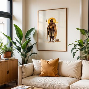 May include: A framed wall art print featuring a watercolour illustration of a bearded figure in a brown cloak holding a wooden staff, standing before a golden circular halo. The artwork is displayed in a thin wooden frame on a plain wall.