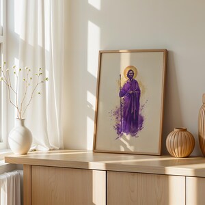 May include: A framed wall art print featuring a watercolor-style illustration of a bearded figure in a purple robe holding a staff, with a golden halo behind the head, set against a light beige background within a simple wooden frame.