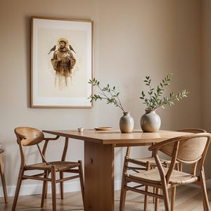 May include: A framed wall art print depicting a figure in brown robes with a golden halo, flanked by two birds, hanging above a wooden dining table with two light-colored ceramic vases containing green leafy branches and two wooden chairs.