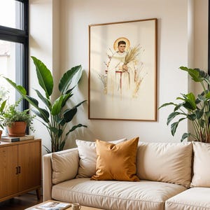 K&ouml;nnte beinhalten: Ein gerahmter Kunstdruck mit einer Aquarellillustration einer Figur in einem wei&szlig;en Gewand mit roter Sch&auml;rpe und goldenem Heiligenschein, die einen Palmwedel h&auml;lt. Die Figur ist von zarten botanischen Elementen auf hellcremefarbenem Grund umgeben.