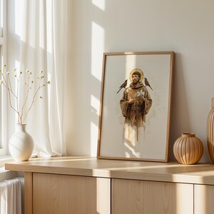 May include: A framed vertical print depicting a figure in a brown robe with a gold halo, holding a white flower with birds perched on the shoulders. The artwork is displayed on a wooden surface alongside a white vase and two ribbed wooden vases.