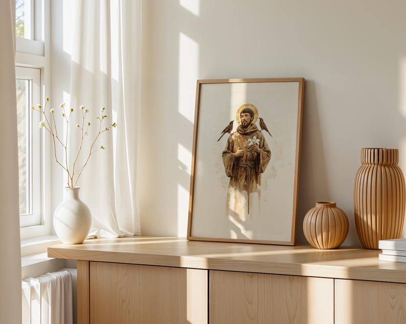 May include: A framed vertical print depicting a figure in a brown robe with a gold halo, holding a white flower with birds perched on the shoulders. The artwork is displayed on a wooden surface alongside a white vase and two ribbed wooden vases.