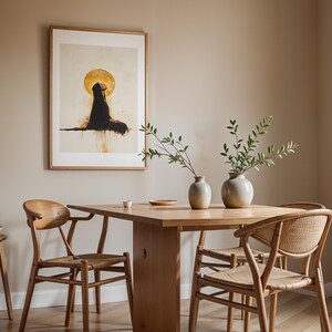 May include: A rectangular framed wall art print featuring a figure in a black robe beneath a large gold circle, displayed above a wooden dining table with two light-coloured ceramic vases containing green leafy branches and three wooden chairs.
