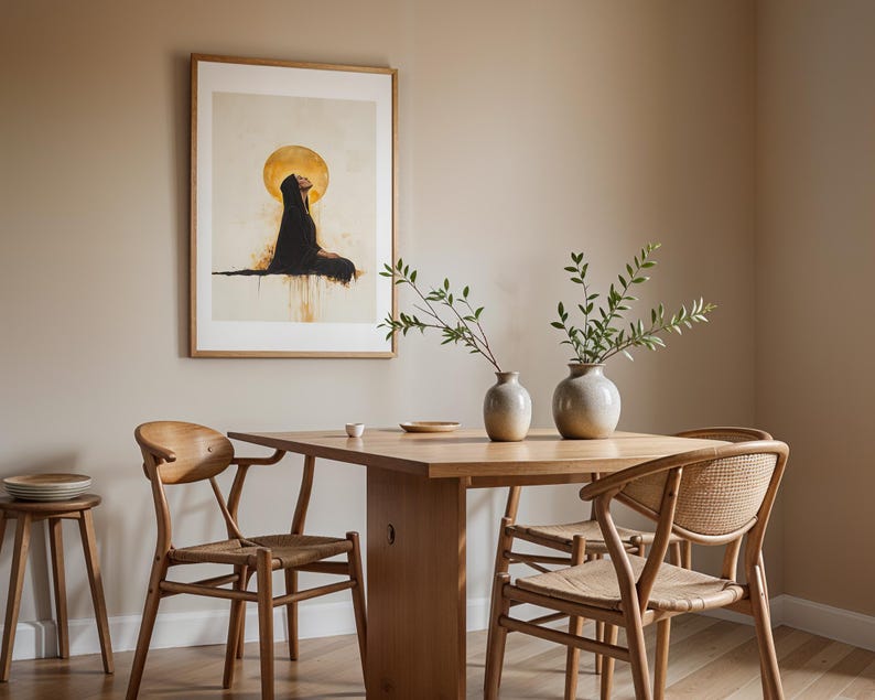 May include: A rectangular framed wall art print featuring a figure in a black robe beneath a large gold circle, displayed above a wooden dining table with two light-coloured ceramic vases containing green leafy branches and three wooden chairs.