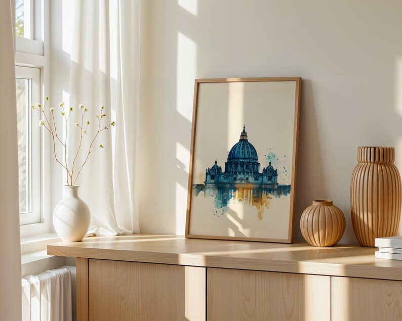 May include: A framed wall art print featuring a watercolour illustration of a large domed cathedral in shades of blue and gold. The artwork depicts the architectural structure with a reflective effect at the base, set against a light cream background.