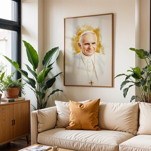 Pu&ograve; includere: Un ritratto incorniciato di Papa Giovanni Paolo II con un effetto alone dorato in stile acquerello dietro la testa. Il soggetto indossa una talare bianca e una croce pettorale d'oro. L'opera &egrave; esposta su una parete sopra un divano beige.