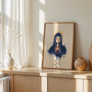 May include: A framed wall art print featuring a watercolor-style illustration of a figure with closed eyes, wearing a dark blue hooded cloak, with a glowing golden halo and a vibrant red heart centered on the chest, set against a cream background.