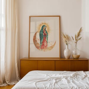 Puede incluir: Una l&aacute;mina de arte enmarcada que presenta una ilustraci&oacute;n en acuarela de la Virgen de Guadalupe sobre una luna creciente, rodeada por un halo dorado, con un manto color verde azulado y un vestido rojo, en un marco de madera clara.