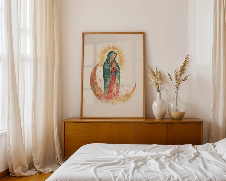 Puede incluir: Una l&aacute;mina de arte enmarcada que presenta una ilustraci&oacute;n en acuarela de la Virgen de Guadalupe sobre una luna creciente, rodeada por un halo dorado, con un manto color verde azulado y un vestido rojo, en un marco de madera clara.