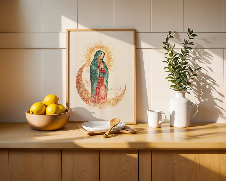 Puede incluir: Una l&aacute;mina de arte enmarcada con una ilustraci&oacute;n en acuarela de la Virgen de Guadalupe sobre una luna creciente con un halo dorado, expuesta junto a un cuenco de madera con limones amarillos, un plato blanco y un jarr&oacute;n blanco.