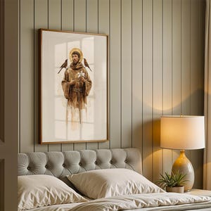 May include: A framed vertical wall art print depicting a figure in a brown hooded robe with a golden halo, holding white flowers with birds perched on the shoulders, rendered in a soft watercolour style with muted earth tones and light shading.