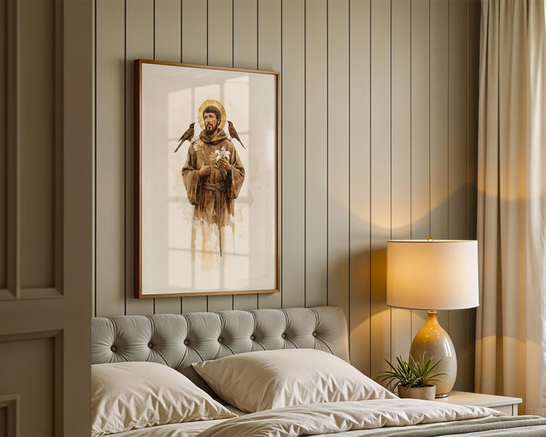 May include: A framed vertical wall art print depicting a figure in a brown hooded robe with a golden halo, holding white flowers with birds perched on the shoulders, rendered in a soft watercolour style with muted earth tones and light shading.