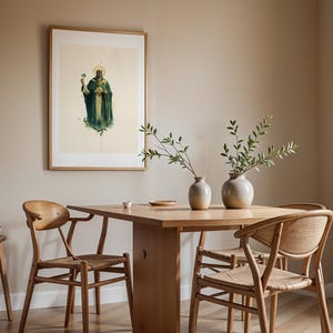 May include: A framed wall art print depicting a figure in a dark green robe and crown holding a shamrock, displayed above a wooden dining table with two light-colored ceramic vases containing green leafy branches and two wooden chairs.