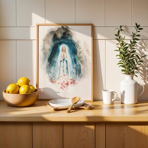 Peut inclure: Une impression aquarelle encadr&eacute;e repr&eacute;sentant une silhouette v&ecirc;tue d'une robe blanche et bleue, les mains jointes en pri&egrave;re, entour&eacute;e d'une grotte bleu fonc&eacute; et de p&eacute;tales de fleurs rouges. L'&oelig;uvre est pos&eacute;e sur un comptoir en bois pr&egrave;s de citrons.