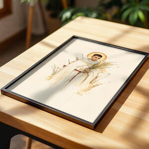K&ouml;nnte beinhalten: Ein gerahmter Druck mit einer Aquarellillustration einer Figur in einem wei&szlig;en Gewand mit goldenem Heiligenschein, die einen Palmwedel h&auml;lt. Die Figur ist von stilisierten Weizenhalmen und getrockneten Gr&auml;sern vor cremefarbenem Hintergrund umgeben.