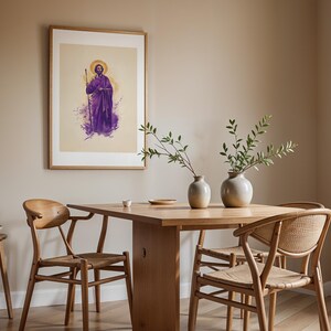 May include: A framed wall art print featuring a figure in purple robes holding a staff with a golden halo, displayed above a wooden dining table with two ceramic vases containing green branches and three wooden chairs with woven seats.