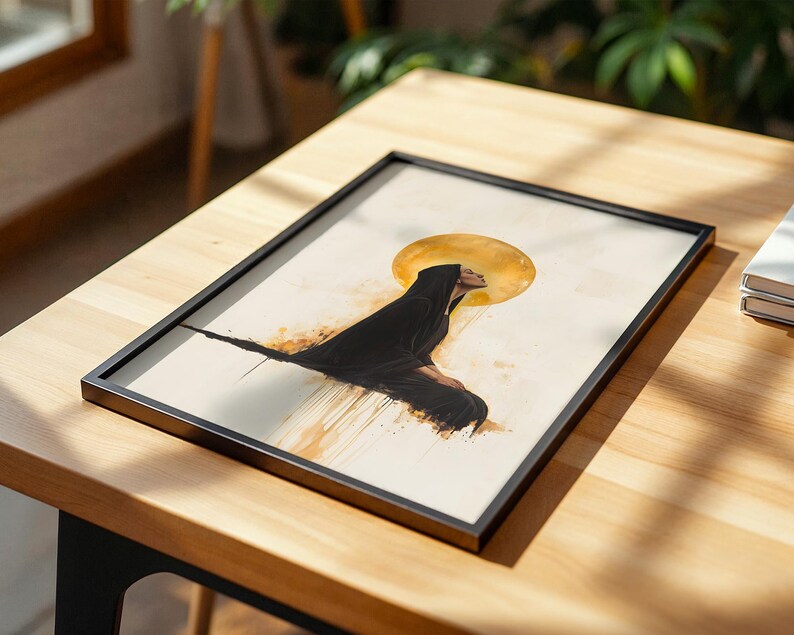 May include: A framed rectangular print featuring a side profile illustration of a figure wearing a black hooded cloak. Behind the figure is a large, circular golden sun or halo. The artwork includes abstract golden paint drips on a cream background.