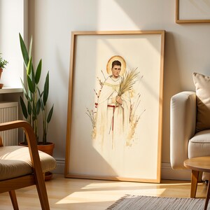 K&ouml;nnte beinhalten: Ein gerahmter vertikaler Wandkunstdruck mit einer Aquarellillustration einer Person in einem wei&szlig;en Gewand mit rotem Kordelg&uuml;rtel, die einen Palmwedel h&auml;lt. Die Figur hat einen goldenen Heiligenschein und ist von stilisierten Weizenhalmen umgeben.