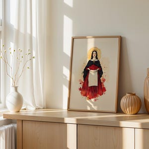 K&ouml;nnte beinhalten: Ein gerahmter Kunstdruck mit der zentralen Illustration einer Figur mit dunklem Haar, goldenem Heiligenschein und Krone, die einen schwarzen Umhang &uuml;ber einem roten Rock tr&auml;gt und eine wei&szlig;e, mit roten Rosen gef&uuml;llte Sch&uuml;rze vor beigem Hintergrund h&auml;lt.
