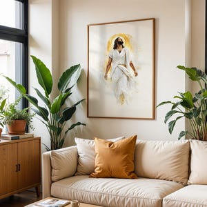 May include: A framed wall art print featuring a figure with long hair and a beard, dressed in flowing white robes, depicted in a watercolor style with a golden circular halo behind the head, set against a light cream-colored background.