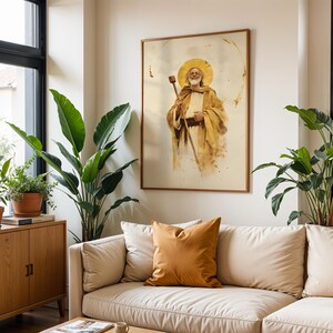 Puede incluir: Una impresi&oacute;n art&iacute;stica enmarcada que presenta una ilustraci&oacute;n estilo acuarela de una figura barbuda con un halo dorado, vistiendo t&uacute;nicas color canela y sosteniendo un bast&oacute;n de madera. La obra se exhibe en una pared clara sobre un sof&aacute; beige con un coj&iacute;n mostaza.
