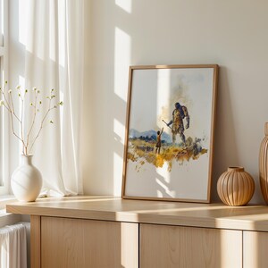 May include: A framed watercolour print featuring a small figure reaching towards a large, towering giant in a golden-hued landscape. The artwork uses expressive brushstrokes in shades of yellow, brown, and blue to depict the scene on a white background.