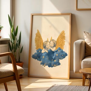 May include: A framed wall art print featuring two cherubs with golden wings resting on a dark blue cloud. The cloud is decorated with small yellow stars, and the background of the print is a light cream colour. The frame is made of light-toned wood.