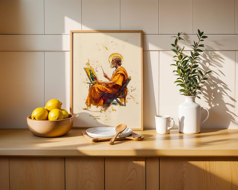 Puede incluir: Una l&aacute;mina enmarcada con una ilustraci&oacute;n en acuarela de una figura barbuda con t&uacute;nica naranja pintando un retrato en un caballete. La obra se exhibe sobre una encimera de madera junto a un cuenco de limones amarillos, un plato blanco y un jarr&oacute;n.