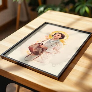 Puede incluir: Una l&aacute;mina enmarcada con una ilustraci&oacute;n estilo acuarela de una persona de pelo corto y oscuro, vestida con una bata m&eacute;dica blanca y un estetoscopio al cuello. Un halo dorado se sit&uacute;a detr&aacute;s de su cabeza y sostiene un bolso de color marr&oacute;n.