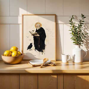 Peut inclure: Une impression d'art encadr&eacute;e repr&eacute;sentant un moine barbu en habit noir tenant un livre ouvert avec une aur&eacute;ole dor&eacute;e au-dessus de la t&ecirc;te et un corbeau noir &agrave; proximit&eacute;. L'illustration est r&eacute;alis&eacute;e dans un style aquarelle sur fond cr&egrave;me.