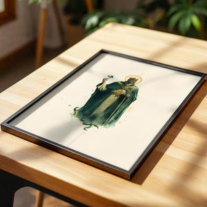 May include: A framed art print featuring a watercolor-style illustration of a bearded figure wearing a dark green robe and a golden halo, holding a small green shamrock in one hand and a circular golden object in the other against a cream background.