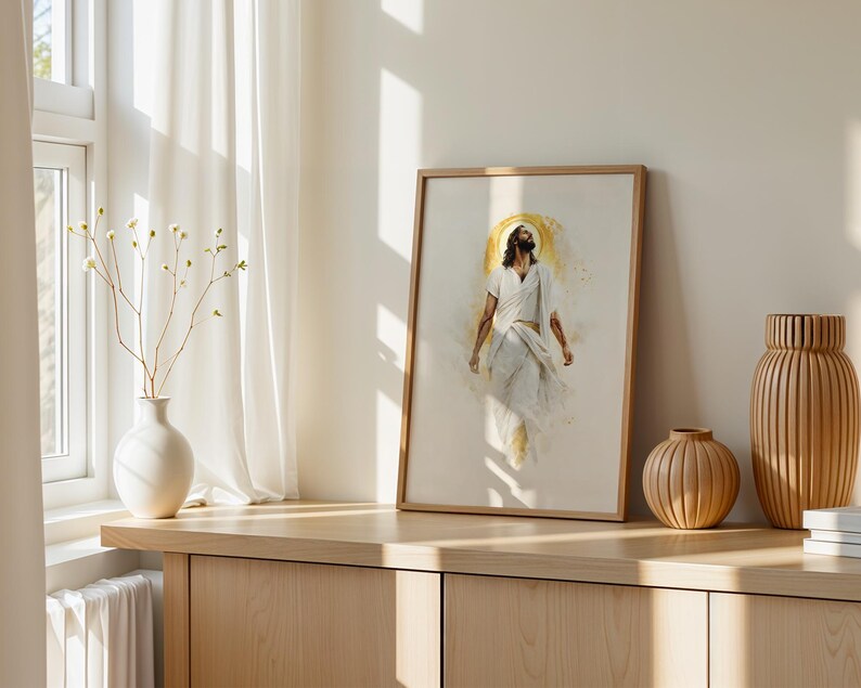 May include: A framed vertical wall art print featuring a watercolor-style illustration of a figure in white robes with a golden halo. The artwork is displayed in a light wood frame, positioned on a wooden surface alongside a white vase and two vases.