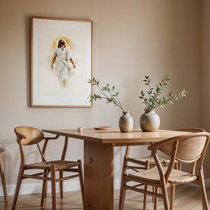 May include: A framed wall art print depicting a figure in white robes with a golden halo, displayed above a wooden dining table with two ceramic vases containing green leafy branches, accompanied by three wooden chairs with woven seats.
