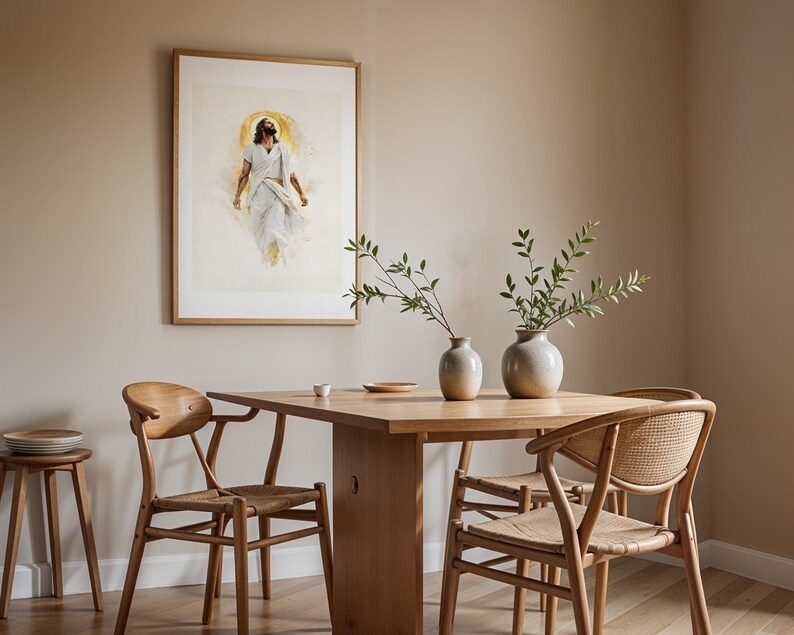 May include: A framed wall art print depicting a figure in white robes with a golden halo, displayed above a wooden dining table with two ceramic vases containing green leafy branches, accompanied by three wooden chairs with woven seats.