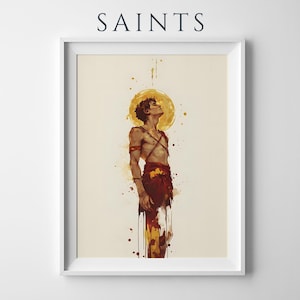 May include: A framed art print titled SAINTS featuring a watercolour-style illustration of a figure with a golden halo looking upward. The figure wears red garments and straps against a cream background with paint splatters in red and yellow tones.