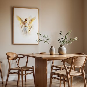 May include: A framed wall art print depicting a figure with large golden wings, holding a staff and a fish, displayed above a wooden dining table with two ceramic vases containing green leafy branches and four wooden chairs with woven seats.