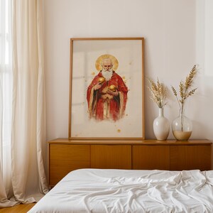 May include: A framed vertical wall art print featuring a watercolour-style illustration of a bearded figure with a golden halo, wearing a red robe and holding two golden spheres, displayed in a light wood frame on a wooden sideboard.