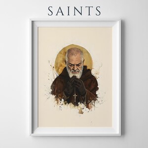 以下が含まれることがあります： SAINTSと題された額入りアートプリント。茶色のフード付きローブを着た髭のある人物が十字架付きのロザリオを持っているイラスト。人物はクリーム色の背景にインクの飛び散り効果が施された円形の金色の光輪の前に描かれています。