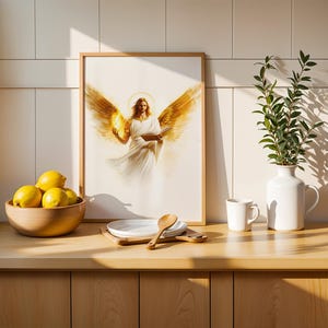 May include: A framed wall art print featuring a central illustration of an angel with large golden wings, a glowing halo, and flowing white robes, holding an open book. The artwork is displayed in a light wood frame on a kitchen counter.