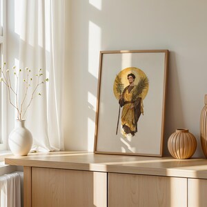 Op de afbeelding: Een ingelijste kunstdruk met een figuur in gouden gewaden die een palmtak en een staf vasthoudt, tegen een cirkelvormige gouden halo. De print staat op een houten oppervlak naast een witte vaas met dunne takken en twee geribbelde houten vazen.