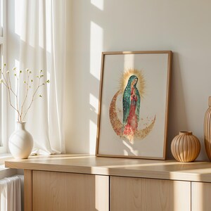Puede incluir: Una l&aacute;mina de arte mural enmarcada con una ilustraci&oacute;n en acuarela de la Virgen de Guadalupe sobre una luna creciente con un halo dorado detr&aacute;s de la cabeza, en tonos verde azulado, rojo y dorado sobre un fondo claro.